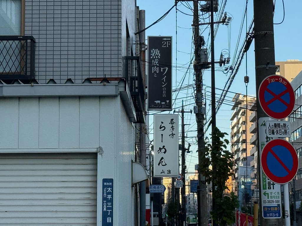 錦糸町の路地に立つ「喜多方食堂 山海」の縦看板と電柱、周囲の街並みの様子