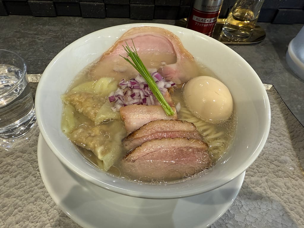 「琥珀の中華蕎麦特上(塩)。透き通ったスープに、3種のチャーシュー、味玉、ワンタン、紫玉ねぎ、三つ葉が盛り付けられた一杯。」