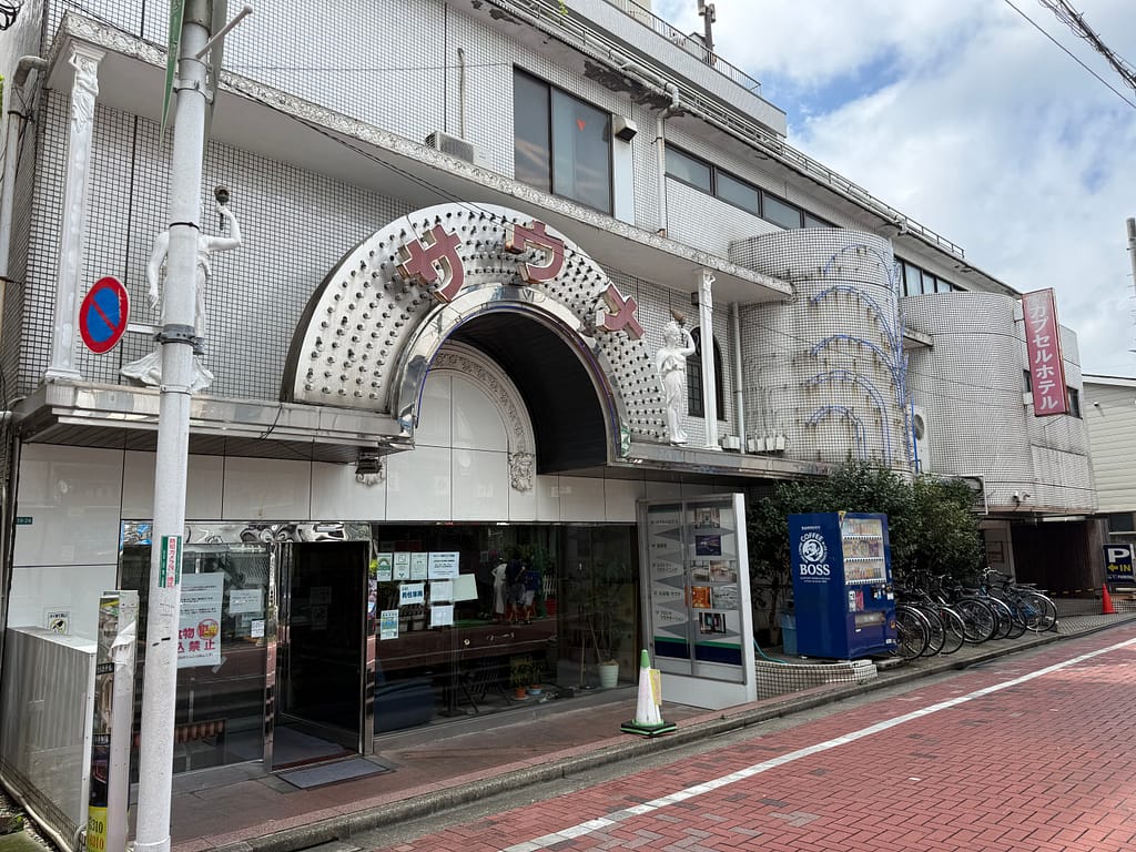 サウナ&カプセルホテルニュー小岩310の店舗外観。アーチ状の「サウナ」看板が目印の建物。