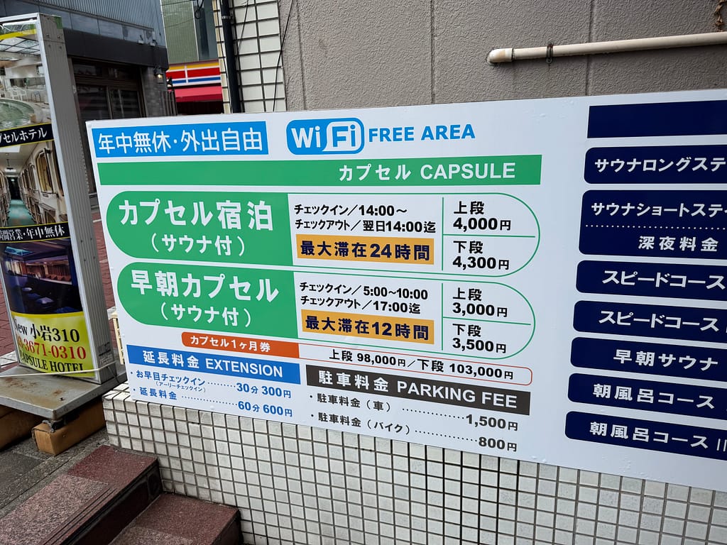 サウナ&カプセルホテルニュー小岩310の館内案内看板。カプセル宿泊や早朝カプセルの料金、チェックイン時間などが記載されている。