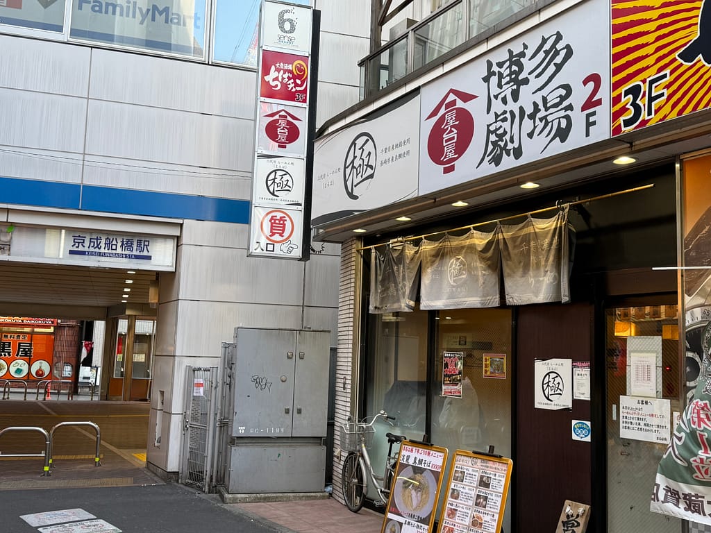 京成船橋駅西口すぐにある三代目麺処まるは極船橋店の外観と店舗入口の写真