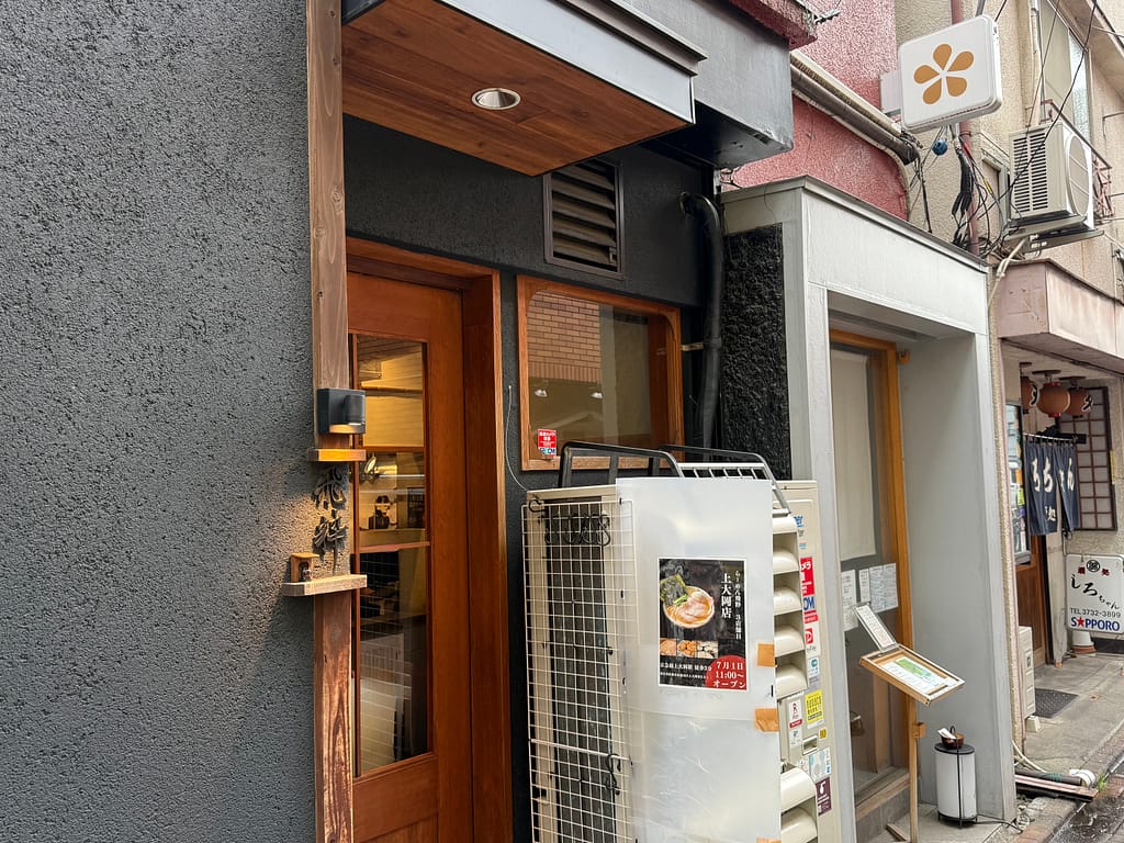 東京都大田区蒲田にある人気ラーメン店「らーめん飛粋 蒲田本店」の外観。黒い外壁に木製の入口が設けられ、店先にはラーメンの案内やメニューが掲示されている。