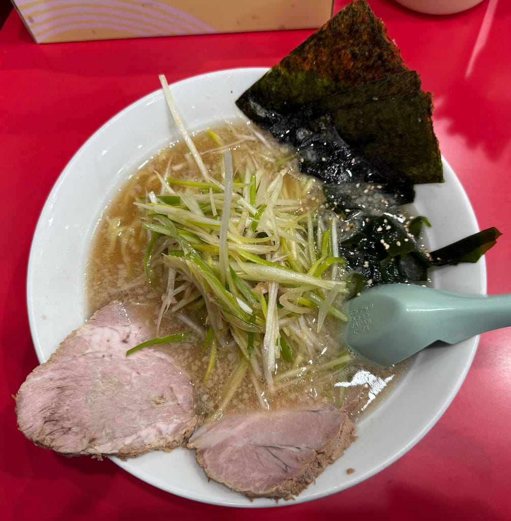 ラーメンかいざん 船橋店の「かいざんラーメン」。山盛りの白髪ネギと海苔、チャーシューが乗った一杯を赤いカウンター席で撮影。