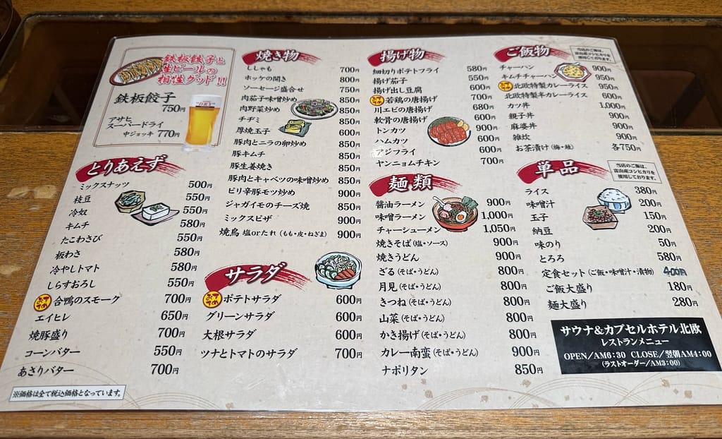 サウナ&カプセルホテル北欧のレストランメニュー表。鉄板餃子やラーメン、定食、揚げ物、サラダなど豊富なラインナップが写真付きイラストと価格表示で並んでいる。