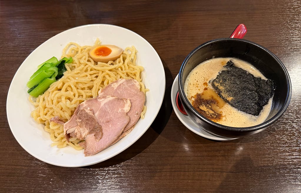 笹本為次郎商店の鶏白湯つけ麺。極太麺にチャーシューや味玉、青菜が添えられ、濃厚で泡立った鶏白湯スープとともに提供されている。