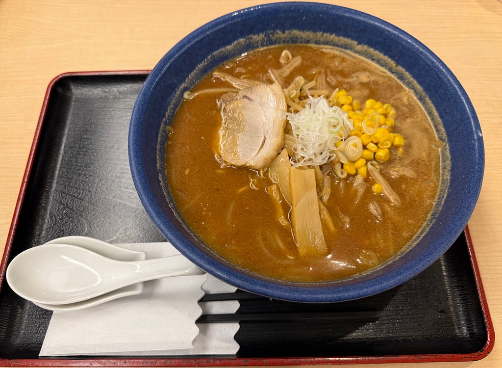 濃厚な味噌スープが香るラーメン。青い丼にチャーシュー、メンマ、もやし、コーン、刻みネギが盛りつけられ、スープの湯気が立ちのぼる一杯。