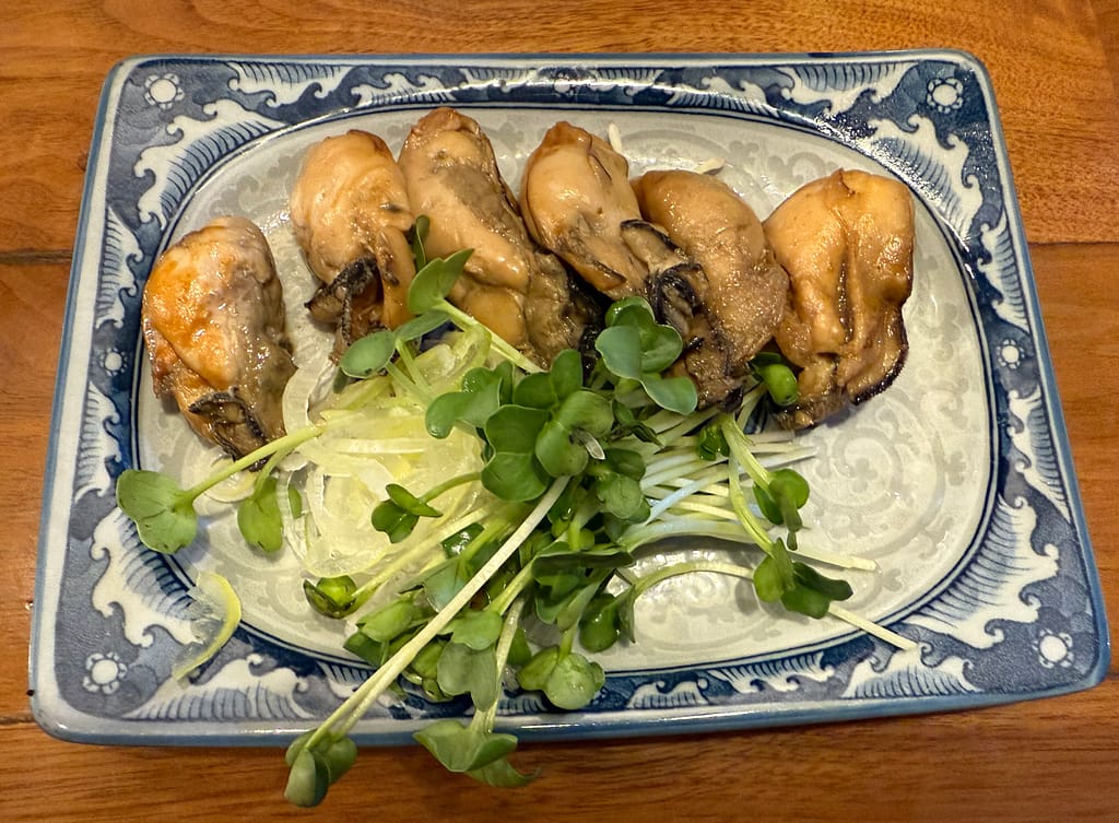 麺や佐市のつまみ牡蠣。ふっくらとした牡蠣が6個、ネギとカイワレが添えられた小皿料理