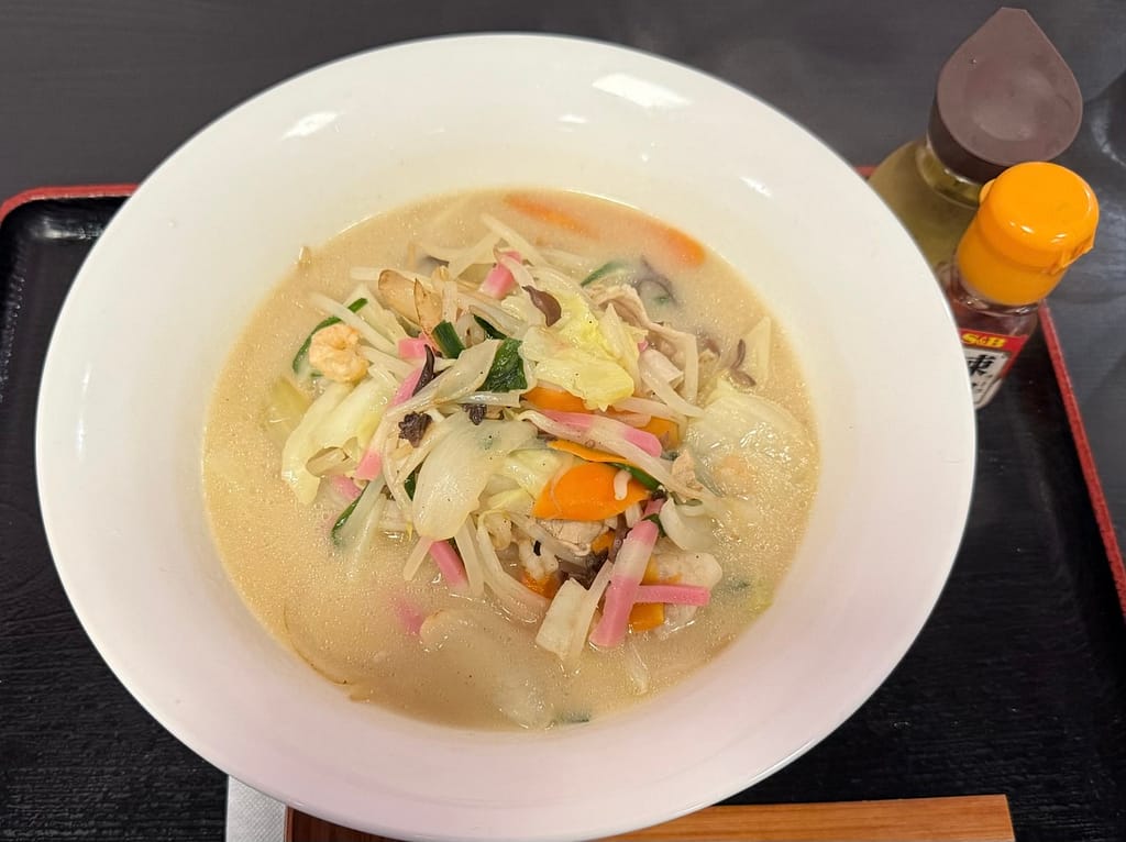 「白濁した豚骨ベースのスープに、キャベツ・にんじん・もやし・きくらげ・かまぼこ・エビなど具材たっぷりのちゃんぽん麺。白い大きめの丼に盛り付けられ、野菜の彩りが映えるボリューム満点の一杯。」