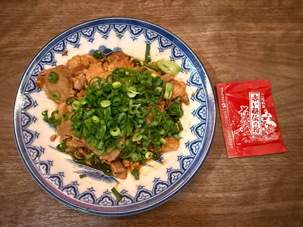 一蘭の煮込み焼豚皿。甘辛く煮込まれた焼豚に刻みネギがたっぷり乗った一品と、特製赤い秘伝の粉。