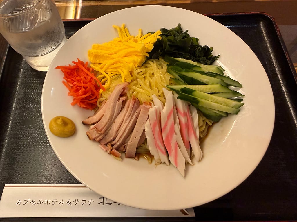 カプセルホテル&サウナ北欧(上野)の冷やし中華。錦糸卵、きゅうり、チャーシュー、なるとなど具材が彩りよく盛り付けられた夏季限定メニュー。