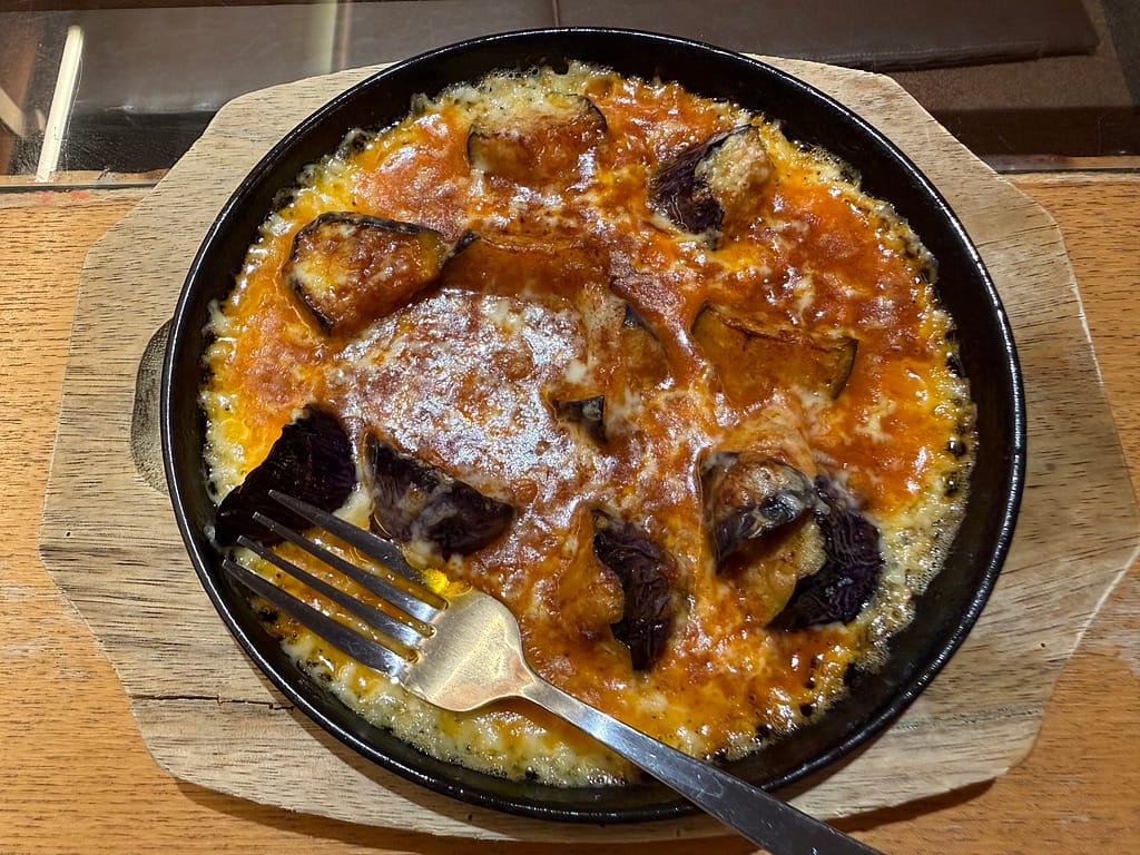 カプセルホテル&サウナ北欧のナスのチーズ焼き。ナスにトマトソースとチーズを合わせて熱々に焼き上げた一品