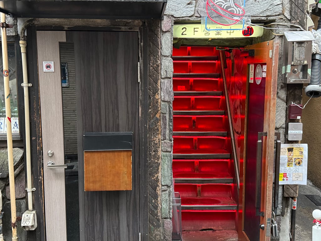 すごい煮干ラーメン凪 新宿ゴールデン街店本館の店舗入口。2階へ続く赤い階段が特徴的な外観。