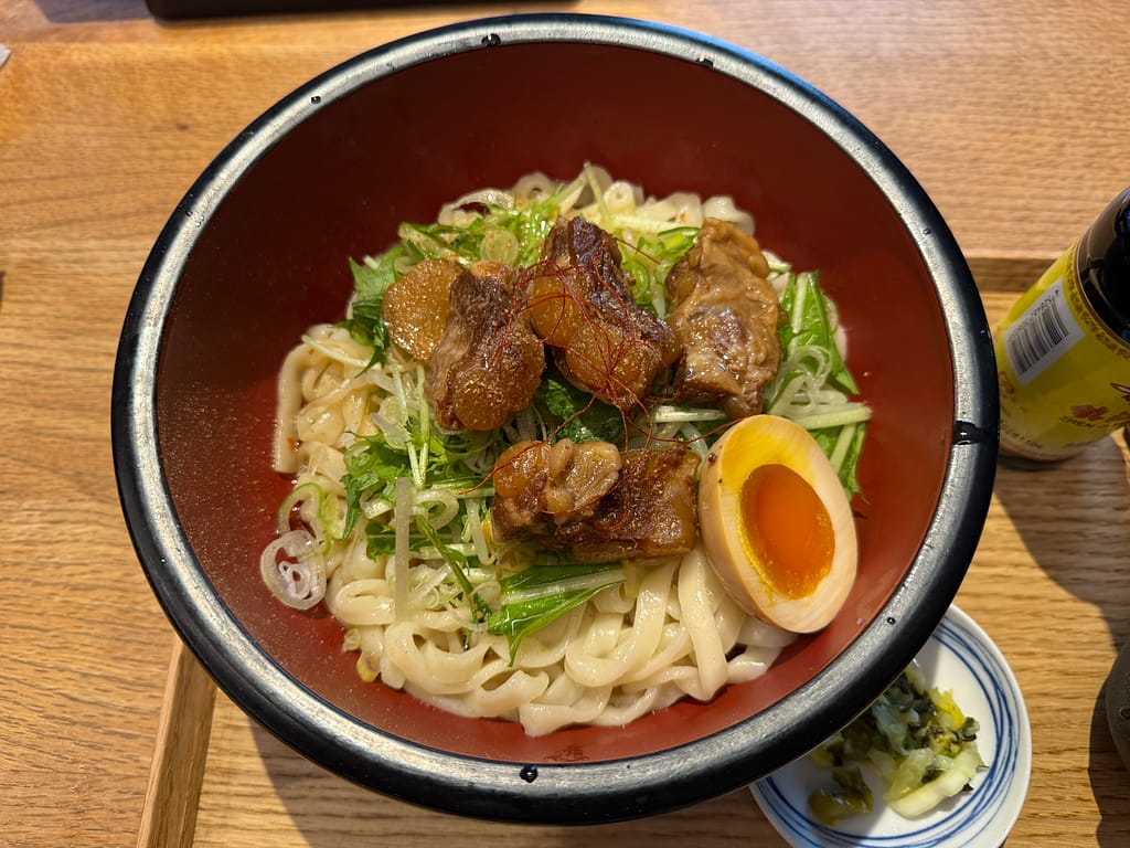 かるまる池袋の『ととのい痺辛パイカうどん』。柔らかなパイカ、半熟味玉、水菜がのった痺れる辛さのうどん。