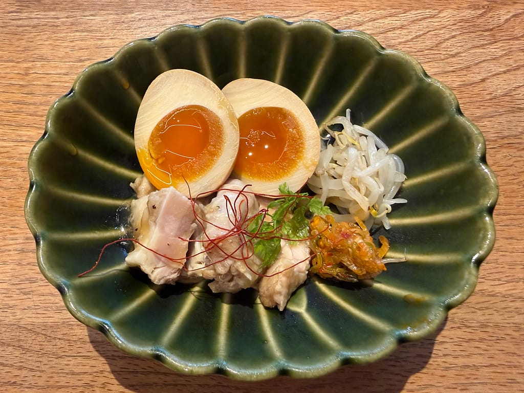 かるまる池袋の『鶏もも味玉ネギ盛り』。しっとりした鶏もも肉、半熟味玉、白ネギを盛り付けた人気のおつまみ。