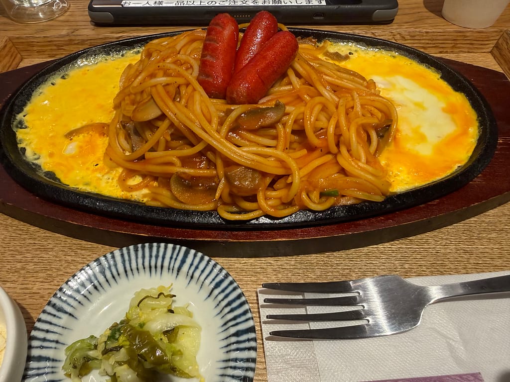 かるまる池袋の『鉄板オムナポリタン』。熱々の鉄板にナポリタンと卵をのせ、ソーセージをトッピングした人気のサ飯。