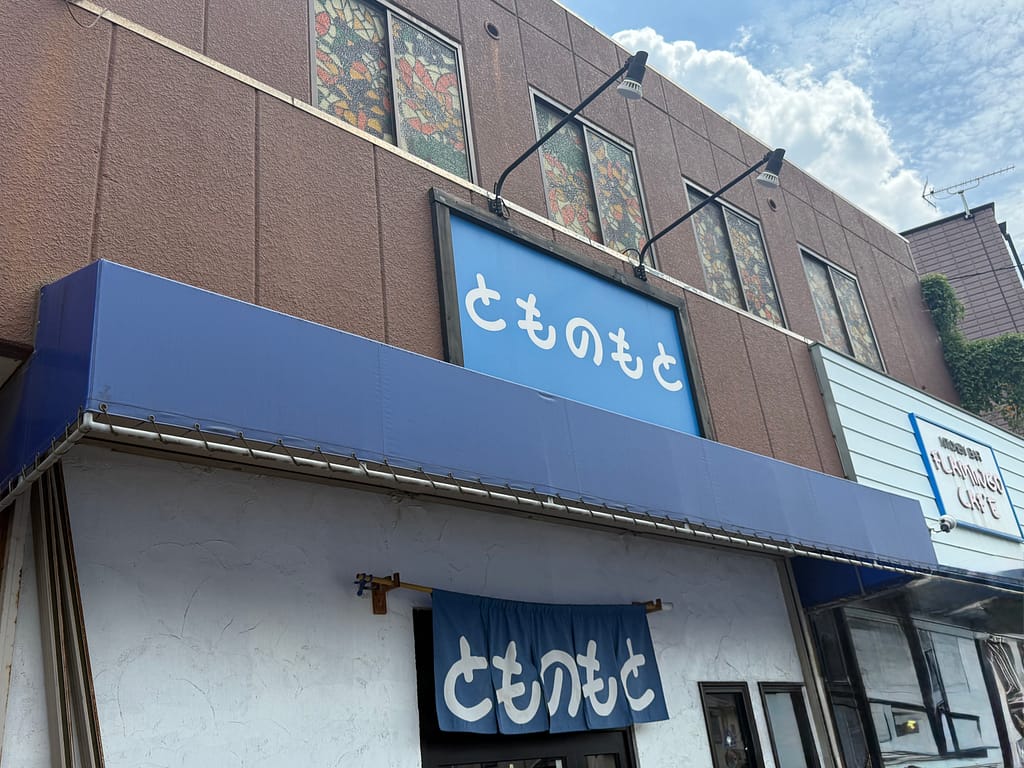 とものもとの店舗外観。青い看板とのれんに「とものもと」と店名が掲げられている。