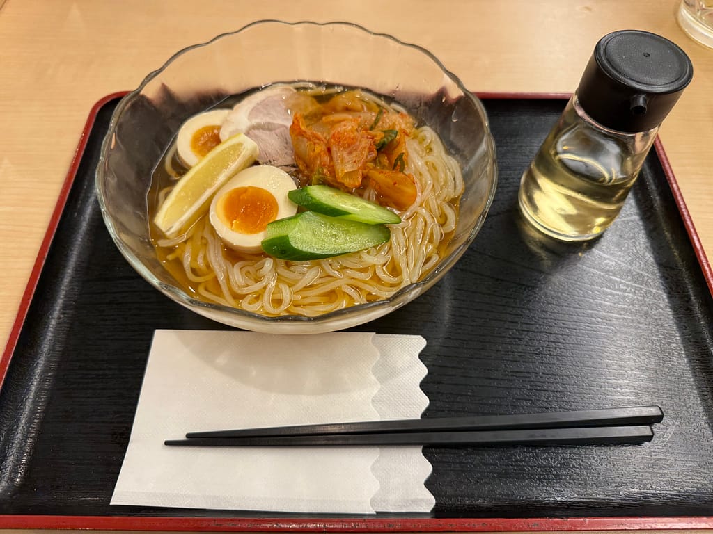 【冷麺】レモン・半熟卵・チャーシュー・キムチ・きゅうりがのった透明感あるスープの冷麺。酸味と辛味のバランスが絶妙な一杯。