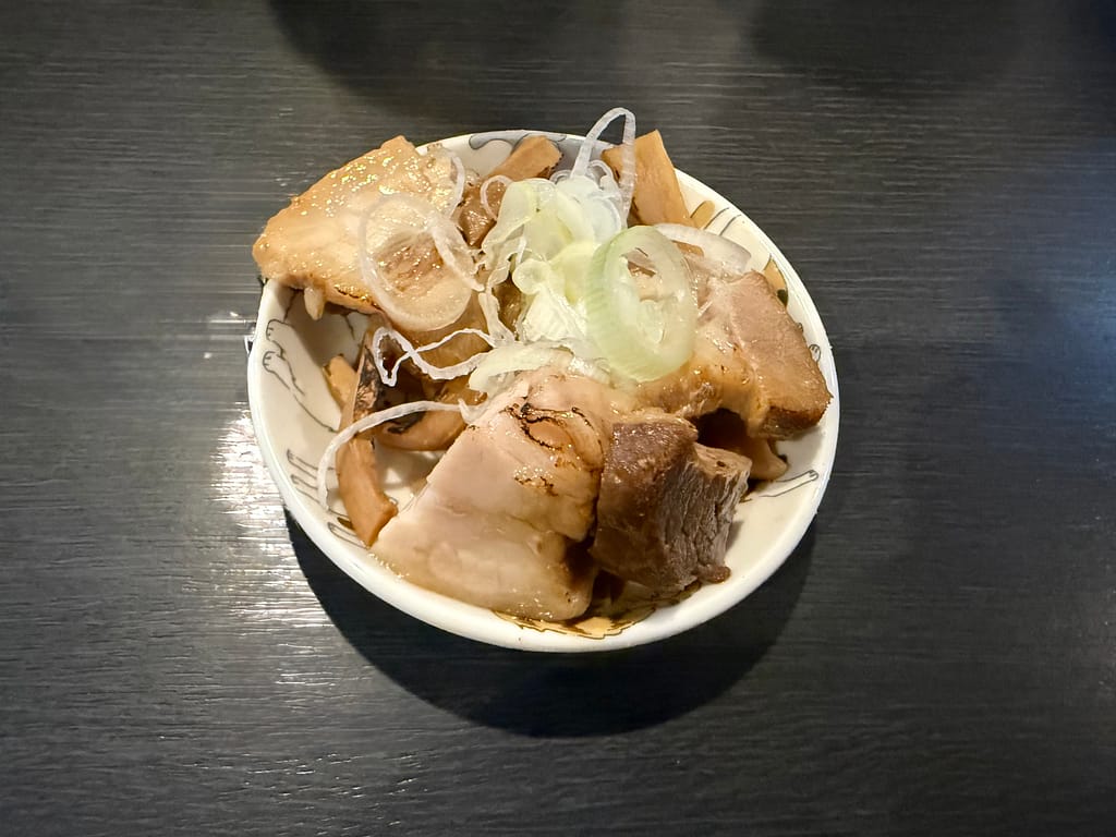 船橋市の自家製麺ご藤で、ビール注文時に提供されるお通し。角切りチャーシューとメンマ、刻みネギを盛り付けた一品。