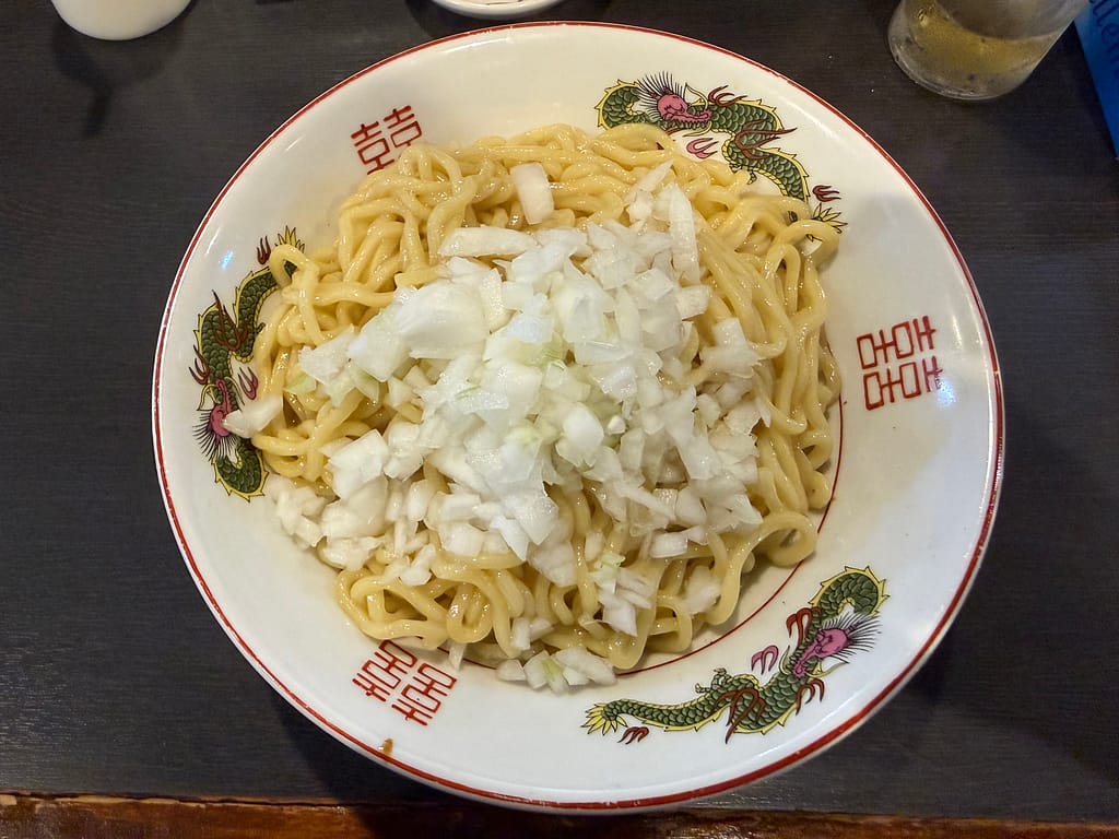 船橋市の自家製麺ご藤の油そば。自家製の太麺に刻み玉ねぎをたっぷりのせた一杯。下にはサイコロ状の角切りチャーシュもたっぷり入っている。