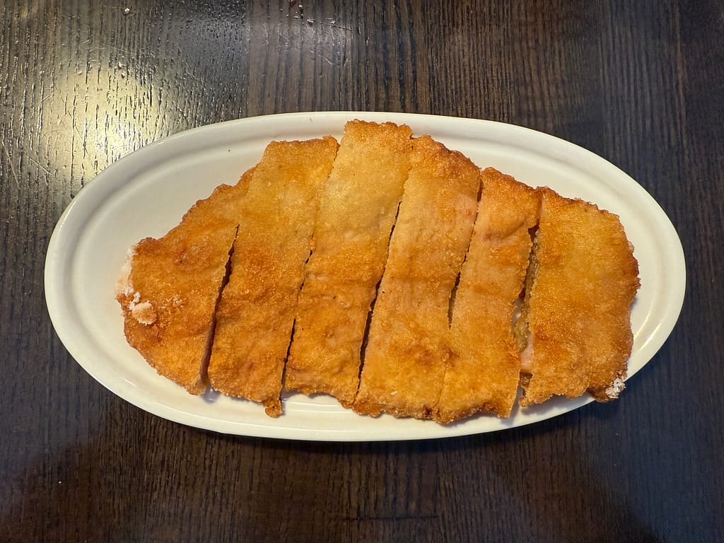 白い楕円皿に盛られたパーコー（豚肉の唐揚げ）。きつね色にカラッと揚がった衣が香ばしく、薄切りの豚肉が５等分にカットされて並んでいる。表面はサクサク、熱々の揚げたてが伝わる見た目。