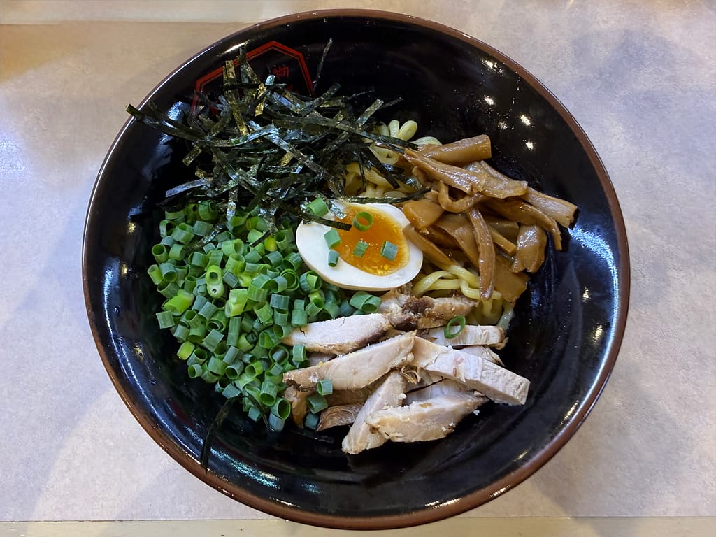 レインボー本八幡で提供される東京名物油そば。もちもちの中太麺に刻みネギ、メンマ、チャーシュー、刻み海苔、半熟味玉が盛り付けられた一杯で、よく混ぜて味わう人気メニュー。