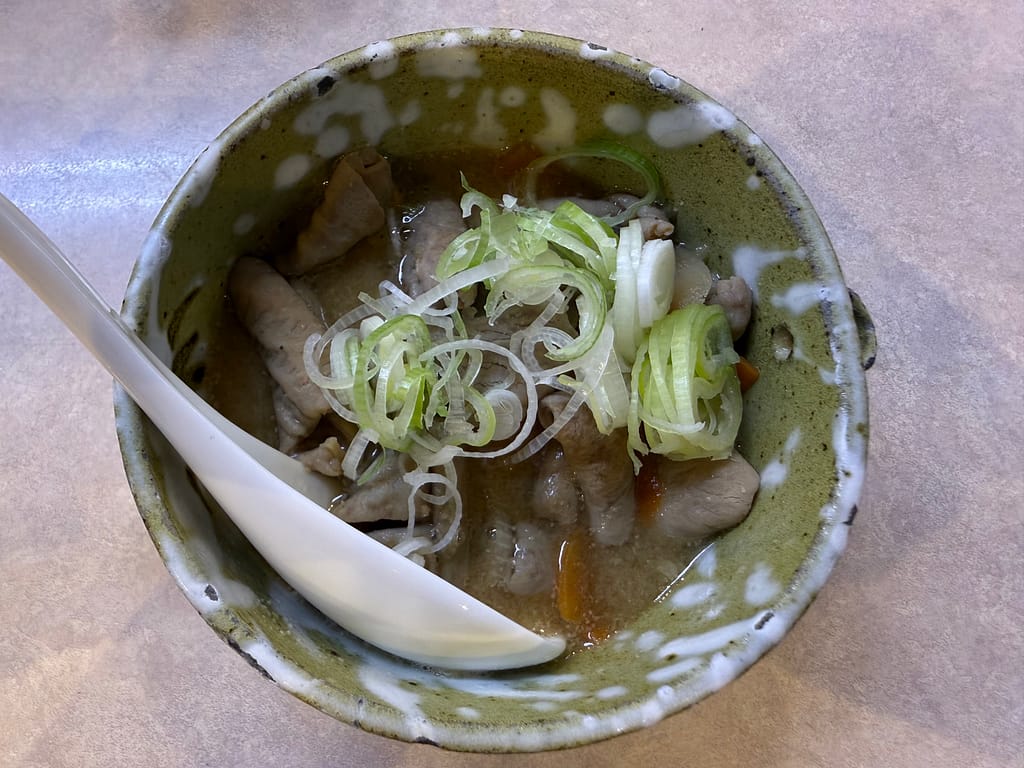 レインボー本八幡で提供されるもつ煮。柔らかく煮込まれたもつに刻みネギを添えた一品で、旨味が溶け込んだ味わい深いスープが特徴のおつまみメニュー。