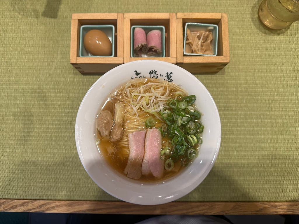 上野・御徒町「らーめん鴨to葱」の特上鴨ラーメン。白い丼に鴨出汁スープ、九条ネギ、鴨肉が美しく盛り付けられ、木箱には煮卵・鴨コンフィ・メンマが添えられている。