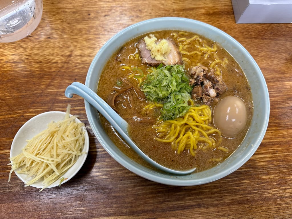 「船橋『温故知新』の味噌ラーメン。濃厚な味噌スープに黄色い中細ちぢれ麺、ネギ・メンマ・チャーシュー・細切れチャーシュー・煮卵がのり、別皿にはたっぷりの針生姜が添えられている。」