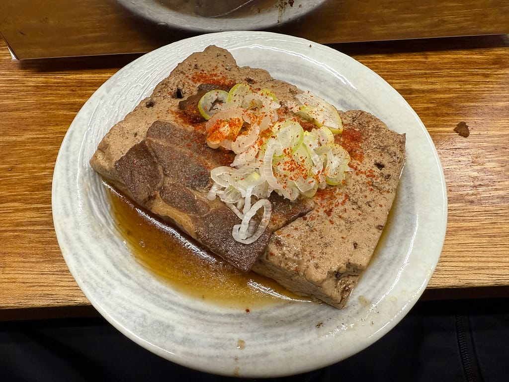 「大衆酒場 若林」で提供される肉豆腐。厚めの豆腐と豚肉があっさりコク深い出汁に浸り、上に刻みネギと一味唐辛子が添えられている。