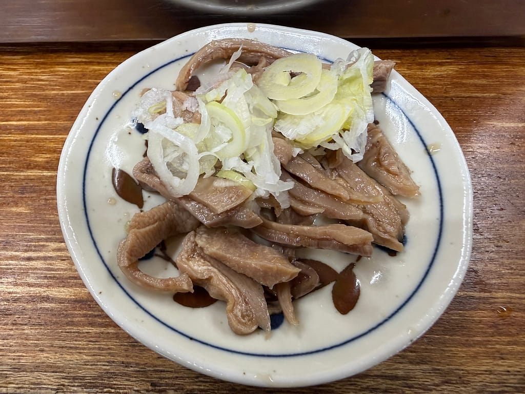 大衆酒場若林のガツにんにく漬け。コリコリ食感の豚ガツに白ネギをのせ、にんにく風味を感じる人気のおつまみ。