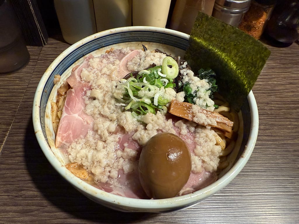 「油カダブラの特製背脂油そば。背脂がたっぷりと降り積もり、チャーシュー、味玉、メンマ、ほうれん草、ネギ、海苔が盛り付けられた濃厚系油そばの写真。」