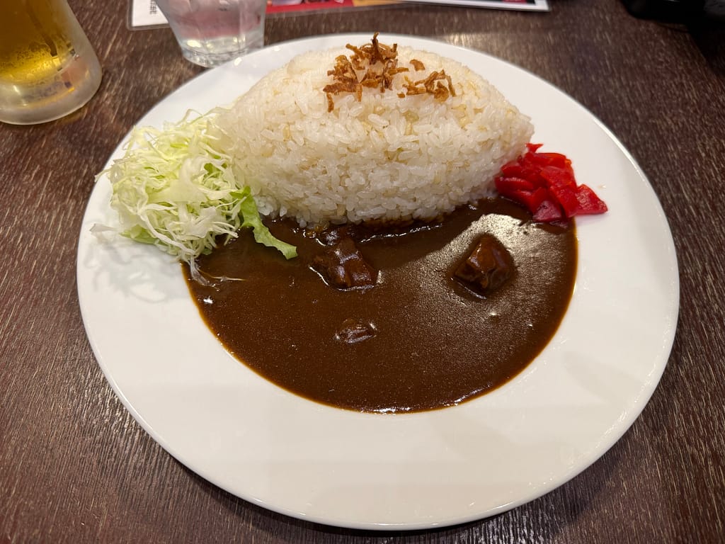 白い皿に盛られたアパホテル名物のビーフカレー。山型に盛られたライスに福神漬けと千切りキャベツが添えられ、濃厚なルーがたっぷりとかけられている。