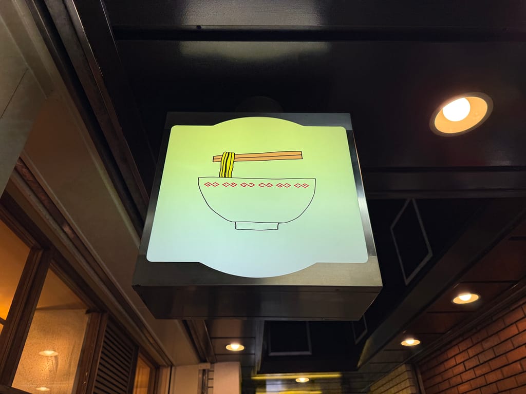 ラーメン丼と箸をモチーフにしたイラスト看板。上野のラーメン店「あいだや」入口付近に掲げられている。
