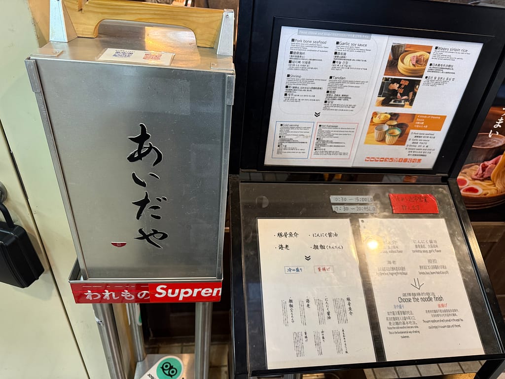 上野のつけ麺専門店「あいだや」の店頭に置かれたメニュー案内。つけ汁の種類や和牛サーロインご飯の説明が掲載されている。
