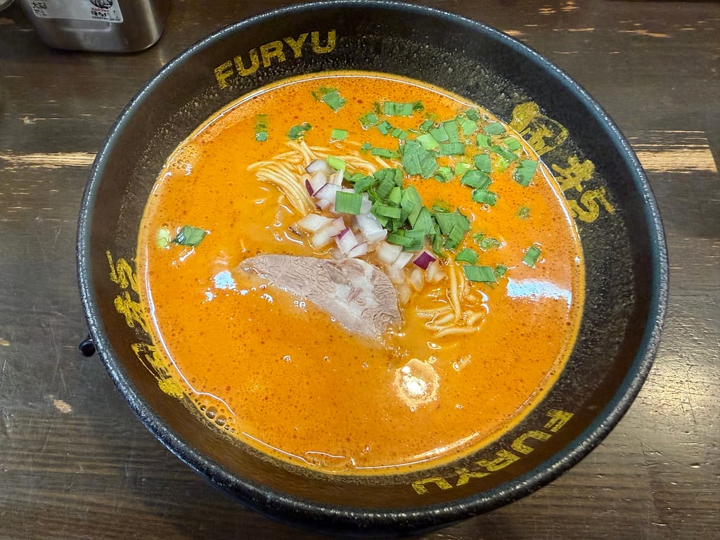 博多風龍 上野店の辛ラーメン。鮮やかな赤い豚骨スープに極細麺、チャーシュー、刻み玉ねぎ、青ねぎがのった一杯。