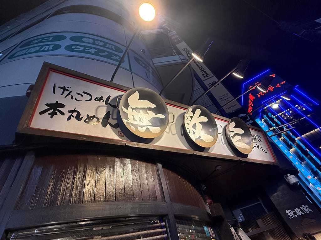 池袋「麺創房 無敵家」の夜の看板をローアングルで撮影した写真。ネオンが輝く深夜の池袋らしい雰囲気が漂う。