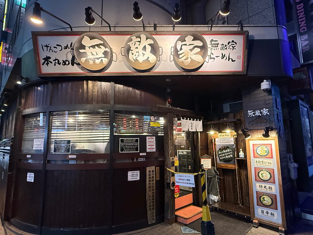 深夜の池袋に佇む「麺創房 無敵家」の外観。大きな看板と温かい照明が印象的で、夜でも賑わいを感じさせる人気ラーメン店。