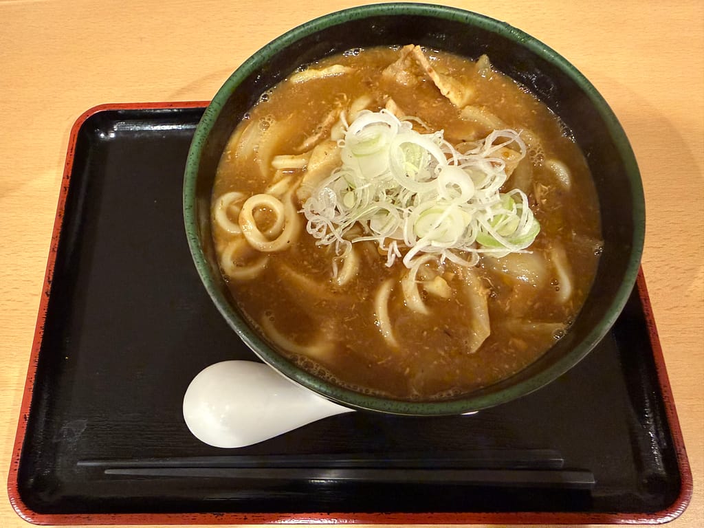 サウナセンター稲荷町のレストランで提供される燻製カレーうどん。燻製の香りが広がる濃厚なカレースープに太めのうどんとたっぷりの白ネギが乗った、サウナ後にぴったりの一杯。