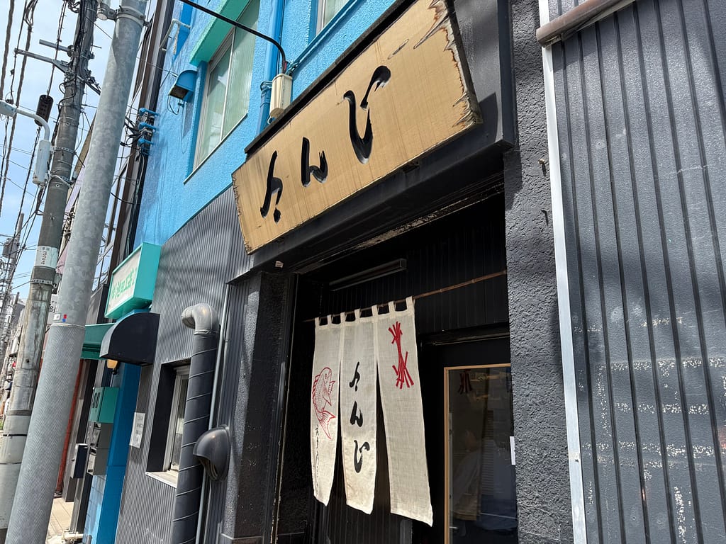 上野の煮干しラーメン店「さんじ」の外観。木製看板とのれんが印象的な店舗入口を斜めから撮影