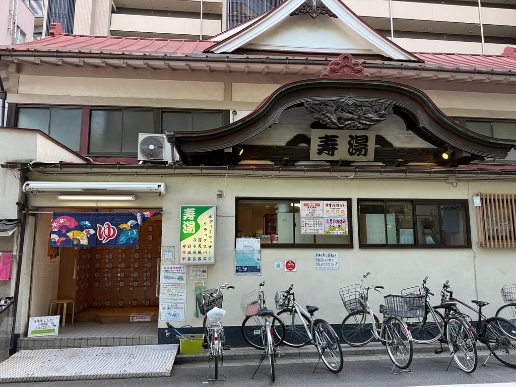 上野の銭湯「寿湯」の建物外観。昔ながらの趣を残す入口と暖簾、自転車が並ぶ様子。