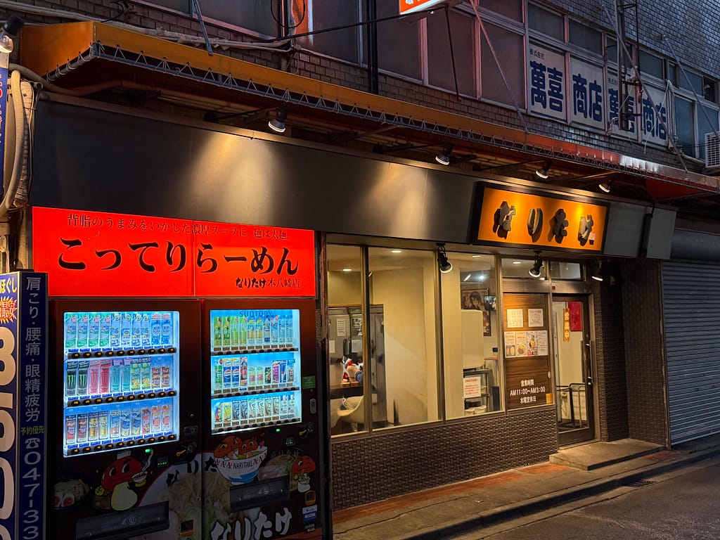 こってりらーめん なりたけ本八幡店の店舗外観、赤い看板と入口が見える夜の様子。