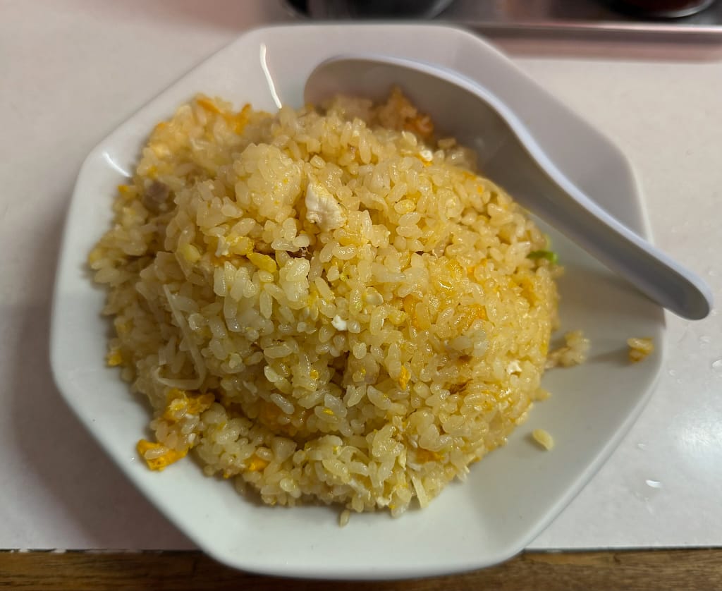 「町中華らしいシンプルな玉子チャーハン。白い皿に盛られ、ふんわりとした玉子と香ばしいご飯が特徴の昔ながらの炒飯。」