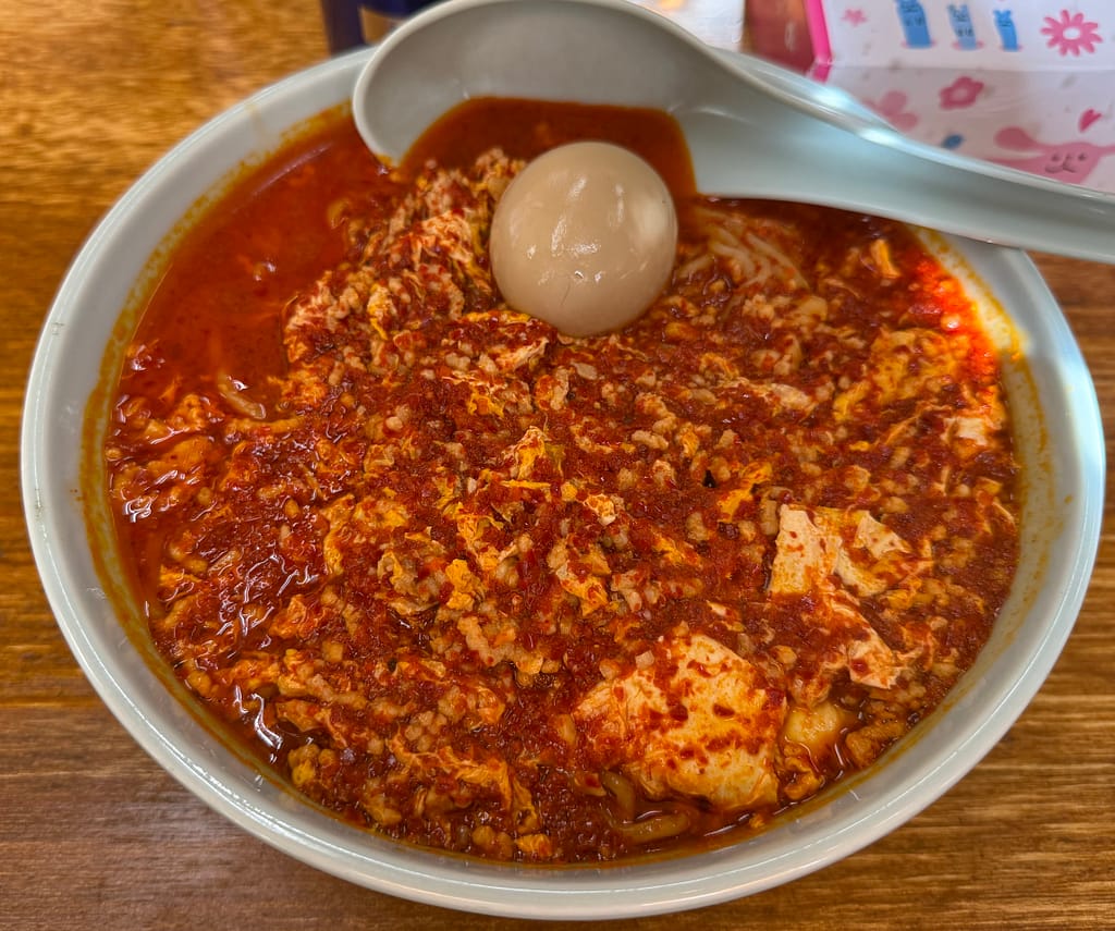 「温故知新の川崎タンタンメン。真っ赤なスープに溶き卵が広がり、中央に味玉が乗った迫力あるビジュアル。辛さ普通でも赤く染まったパンチのある一杯。」