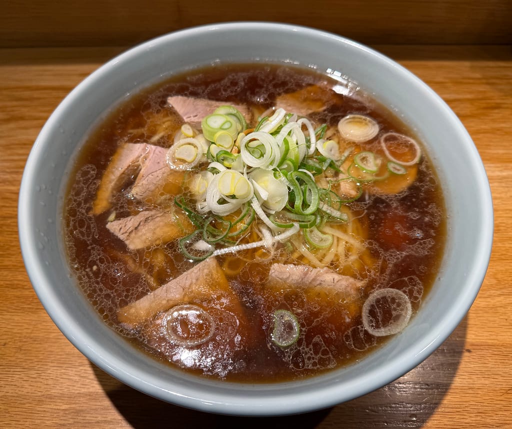 醤油スープにチャーシューと刻みネギがのった中華そばのアップ写真。透き通ったスープに油が浮き、シンプルで王道なビジュアルの一杯