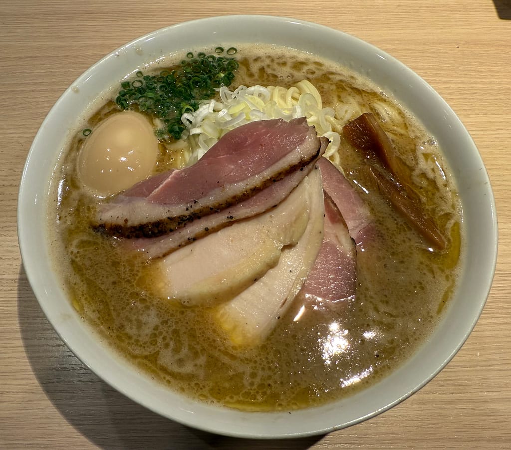 白い丼に盛られた特製濃厚魚介ラーメン。表面に旨味を含んだ濃厚な魚介スープが広がり、チャーシューは鶏と豚の2種類が重ねられている。煮卵、ネギ、メンマが添えられ、香ばしい香りが立ちのぼる一杯。麺屋いっとうの人気メニュー「特製濃厚魚介ラーメン」（1680円）。