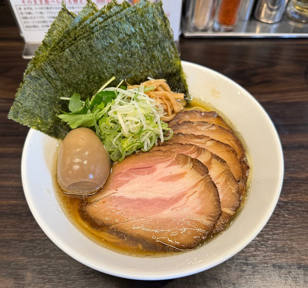 白い丼に、厚いチャーシューが花のように美しく盛り付けられた「特製淡麗（黒）中華そば」。味玉、たっぷりの海苔、刻みネギが添えられ、澄んだ黒醤油スープが輝く上品な一杯。