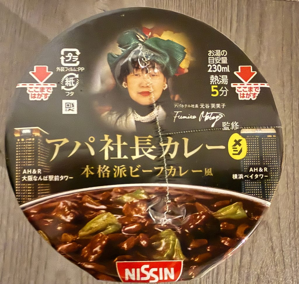 日清食品のカップ食品「アパ社長カレー 多」。元谷芙美子社長の肖像がデザインされたフタと、本格派ビーフカレーをイメージしたパッケージ。
