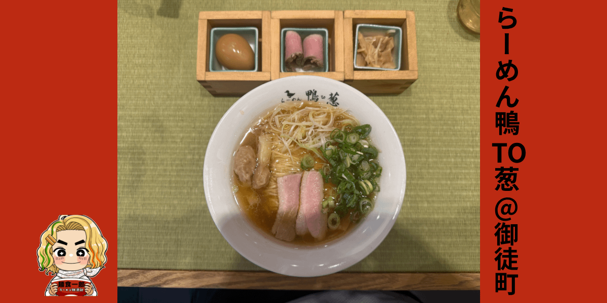 上野・御徒町「らーめん鴨to葱」の特上鴨ラーメンのサムネイル画像。中央に白い丼、上部に木箱入りの煮卵・鴨コンフィ・メンマ、背景は緑の畳テーブル。左下に麺食一郎キャラクター、右側に赤帯で「らーめん鴨TO葱@御徒町」の文字。