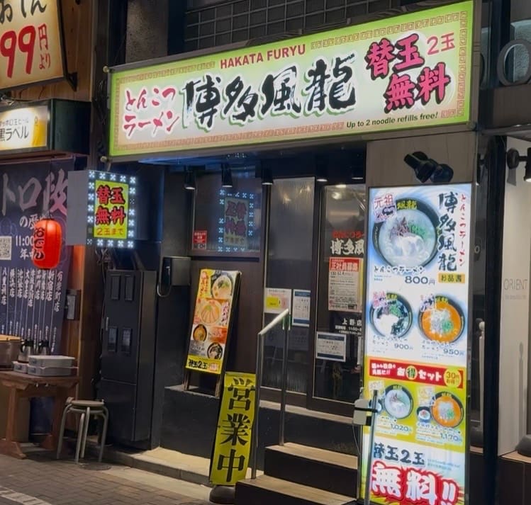 博多風龍 上野店の外観。黄色い看板に「とんこつラーメン 博多風龍」「替玉2玉無料」と大きく書かれ、店頭にはメニュー看板と営業中の立て看板が並ぶ夜の店舗風景。