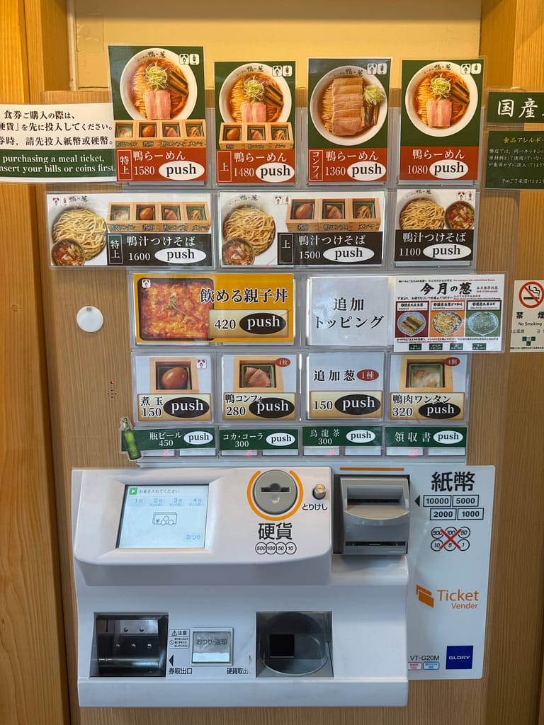 上野・御徒町「らーめん鴨to葱」の食券販売機。鴨ラーメン、特上鴨ラーメン、鴨汁つけそばなどのメニューが並び、ネギの種類や追加トッピングも選べる。